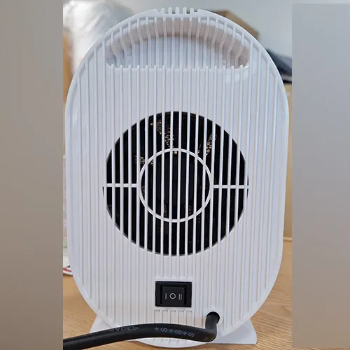 Încălzitor cu ventilator de culoare albă, de formă ovală, prevăzut cu o grilă neagră și un cablu de alimentare de culoare neagră. Produs vândut online, în special prin intermediul Amazon (ASIN: B0CMCZT6QR).