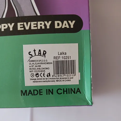 Păpușă din plastic îmbrăcată în blană din fibre sintetice, purtând o pălărie din fibre sintetice, ținând în mână o geantă din plastic dur.