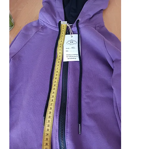 Salopetă pentru copii, confecționată din tricot violet, cu glugă, două buzunare pe față și un șnur cu capete libere, de aproximativ 31 cm lungime.