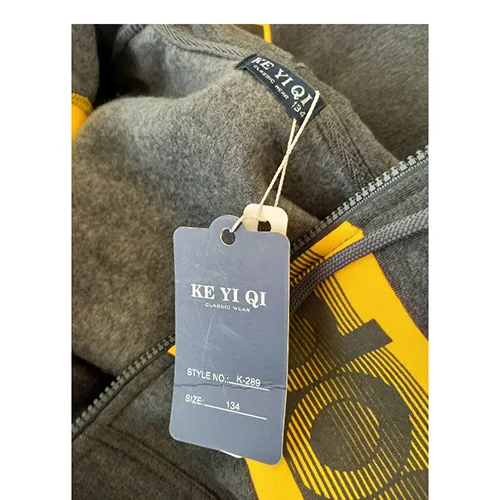 Set de îmbrăcăminte destinat copiilor de vârstă mică, confecționat din material textil tricotat gri. Acesta include un hanorac cu glugă, fermoar și buzunare inserate. Capota are un cordon textil funcțional cu șnur, cu capete libere, de aproximativ 28 cm lungime. Include, de asemenea, o pereche de pantaloni din material tricotat textil albastru deschis și cu buzunare inserate.