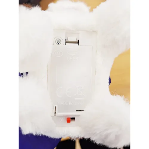 Jucărie electronică de pluș în formă de cățeluș cu panglică roșie și guler cu clopot. Produs vândut online, în special prin intermediul Shein (identificator unic: sl2311262284392222).