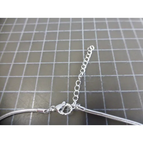 Colier metalic argintiu cu pandantive metalice argintii, negre și aurii, &icirc;nchidere și prelungitor de lanț.