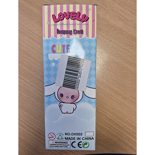 Păpușă din plastic cu o rochie albastră, albă și roșie închisă, păr albastru deschis și o pălărie albă cu urechi.