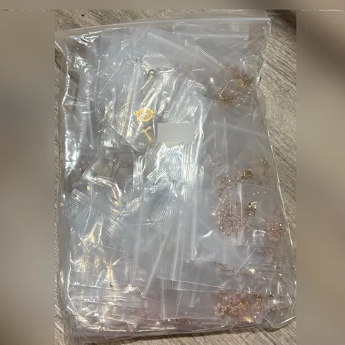 Colier roz cu mărgele de culoare roz, un pandantiv metalic rotund și o cruce metalică, vândute în vrac.