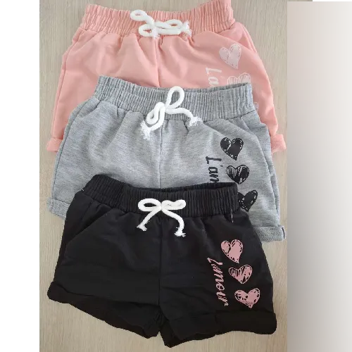 Set de trei perechi de pantaloni scurți destinați copiilor, în diferite culori (gri, roz și negru), cu un design imprimat pe coapsa stângă, precum și un arc decorativ realizat dintr-un șnur alb atașat cu o cusătură în talie. Componența declarată: 95% poliester, 5% elastan.